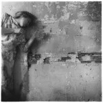 A woman stands against a deteriorating wall.