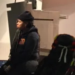 A woman in a beanie sitting on a stage.