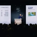 A white man with white hair and black glasses stands behind a podium that reads, "Christie