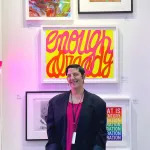 Portrait of Esther McGowan in front of various artworks including a Silence=Death poster.
