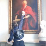 A person spray paints a painting of a white men with red paint.