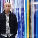 An Asian man standing beside a long blue photograph.