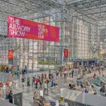 Aerial view of Javits Center, a steel and glass structure, with people waiting in line. Above is a banner that reads 