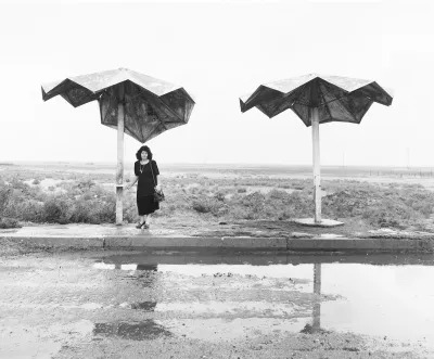A woman standing beneath a metal umbrella.