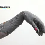 A limp hand with pink nails is in the middle of the frame, covered in a gray viscous substance.