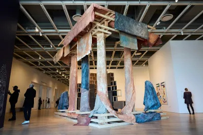 A temple-like structure that is partially deconstructed to reveal an armature beneath it. The structure is draped with brown, grey, and blue paintings.