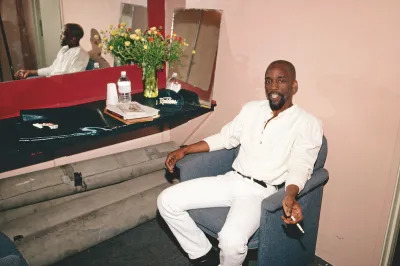 A Black man in a chair smoking a cigarette.