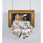 A sculpture of two twin sisters—one light-skinned and blond, the other dark-skinned and black haired—sit on a swing weaing white communion dresses, sneakers, and boxing gloves with the Puerto Rican flag.