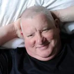 A man lies back on a bed with his hands behind his head.