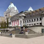 The front exterior of the Vancouver Art Gallery on a sunny day, showing several people sitting on its steps.
