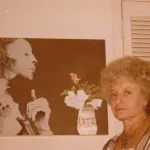 A woman standing beside a large picture of a mummy on a wall.