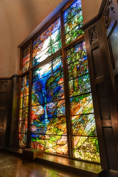 View of a monumental stained-glass window of a mountain landscape with highly saturated color.