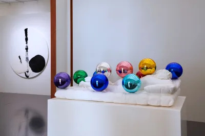 A sculpture of a sleeping nude with polished colored orbs in the foreground and a black and white circular abstract painting hangs on a wall in the background. 