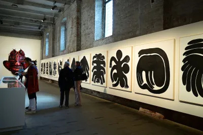 Several people walking by a lined with drawings of abstracted people who sprout multiple arms and appear to bend.
