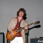A man holding a guitar before an amp.