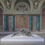 A tangle of stainless-steel creatures--part simian, part human--sits on a low platform in an ornate 18th-century interior.