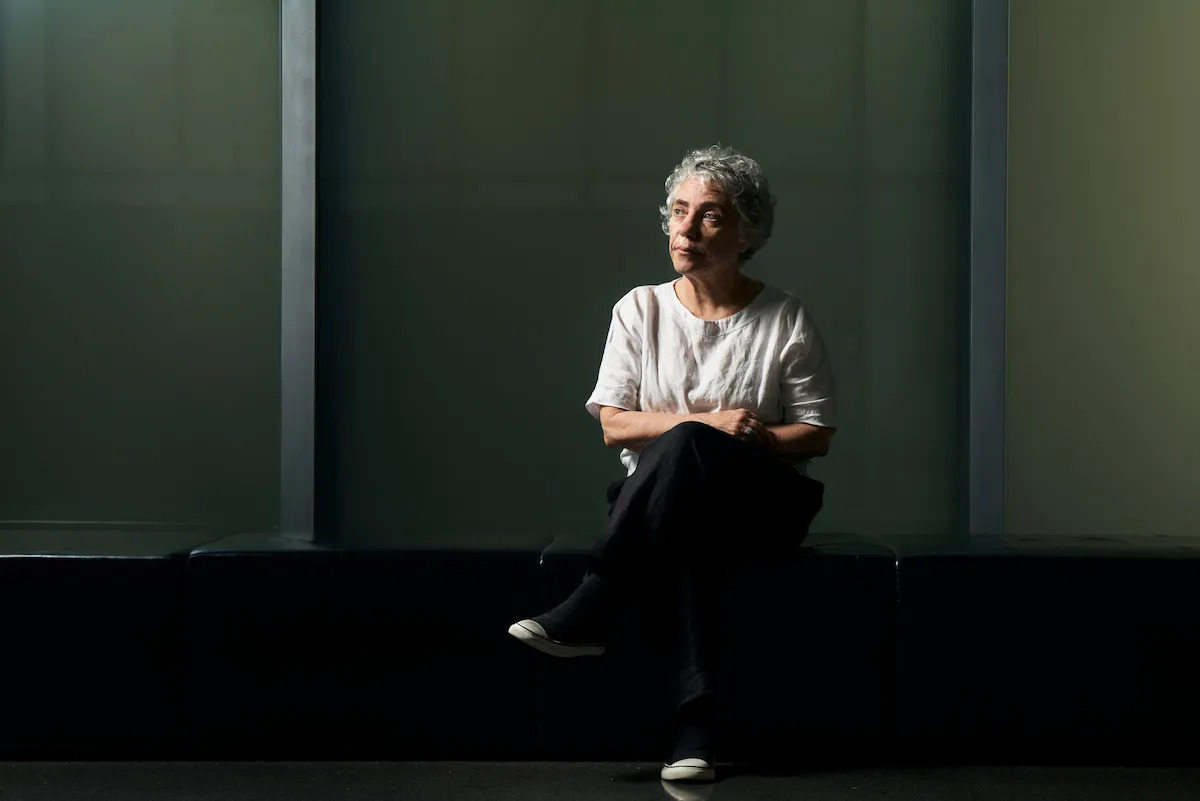 A woman sitting in a darkened space with her legs crossed.