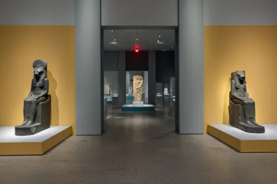 A gallery with two sculptures of seated gods on either side of a hallway.