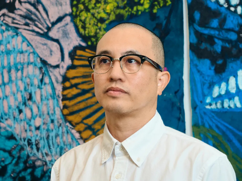 A man with glasses in front of an abstract painting.