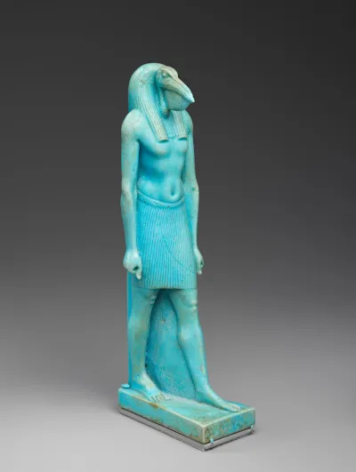 A blue sculpture of a bird-headed man walking with one leg forward.