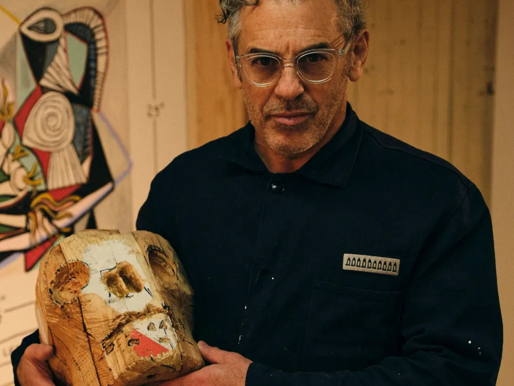 A man in glasses holds a wooden skull.