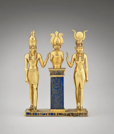 A golden statue of two gods holding one arm each to a central figure with a headdress. The central figure sits on a blue column.