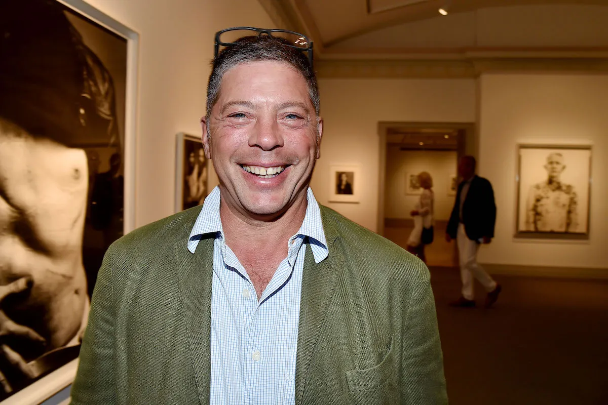 A smiling man in a green leather jacket standing in a gallery.
