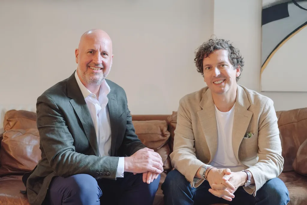 Two men sitting on a sofa smiling.