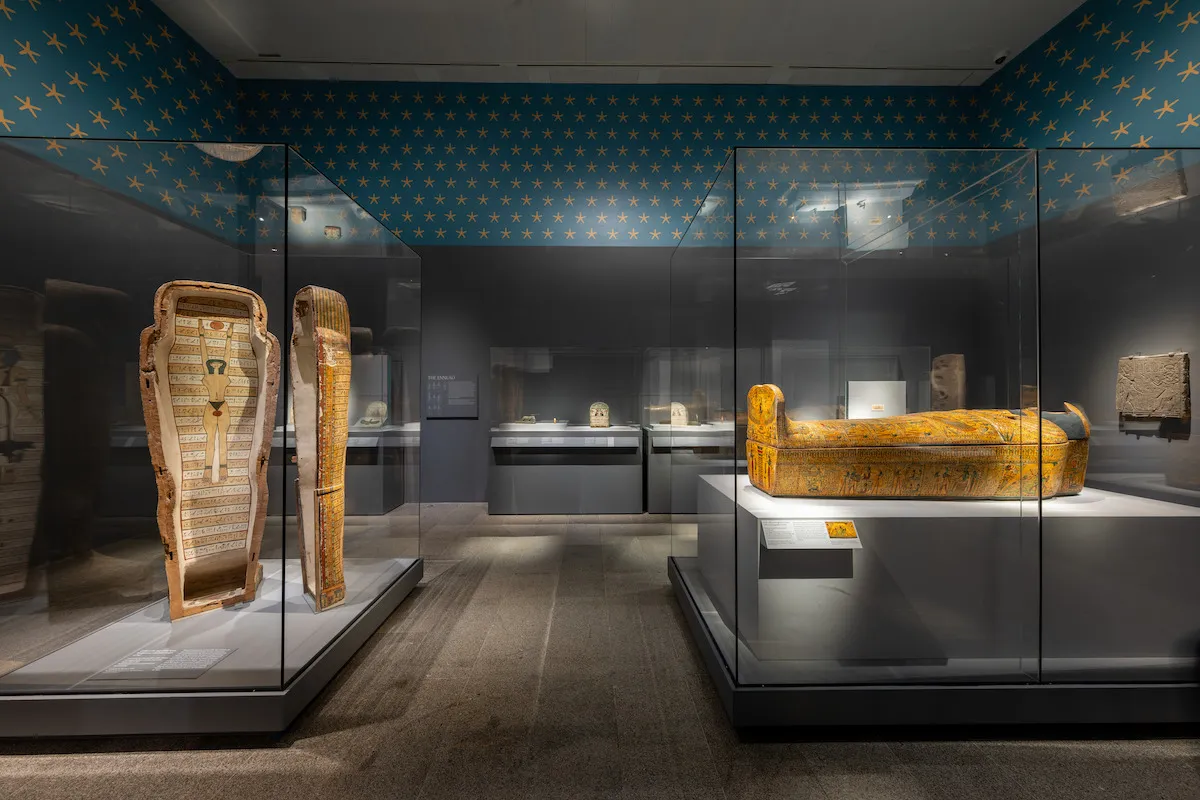 An open sarcophagus and a closed sarcophagus in a gallery with stars painted around the upper parts of its walls.