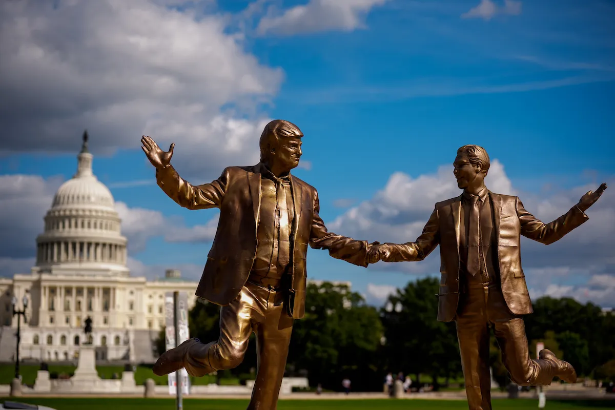 A statue of two men in suits holding hands before a domed building.